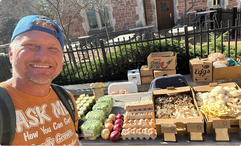 Mushroom Dave smiling behind a market table with produce and mushrooms.